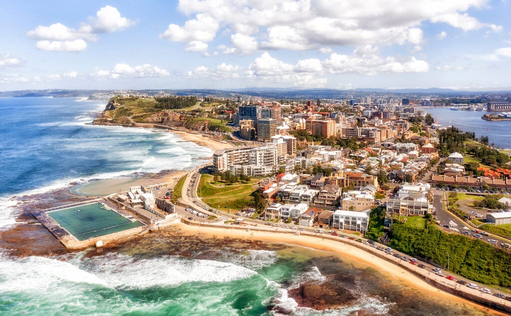 Panorama of Newcastle city on the hills over Hunter river and Pacific ocean with beaches, pool and surfers.